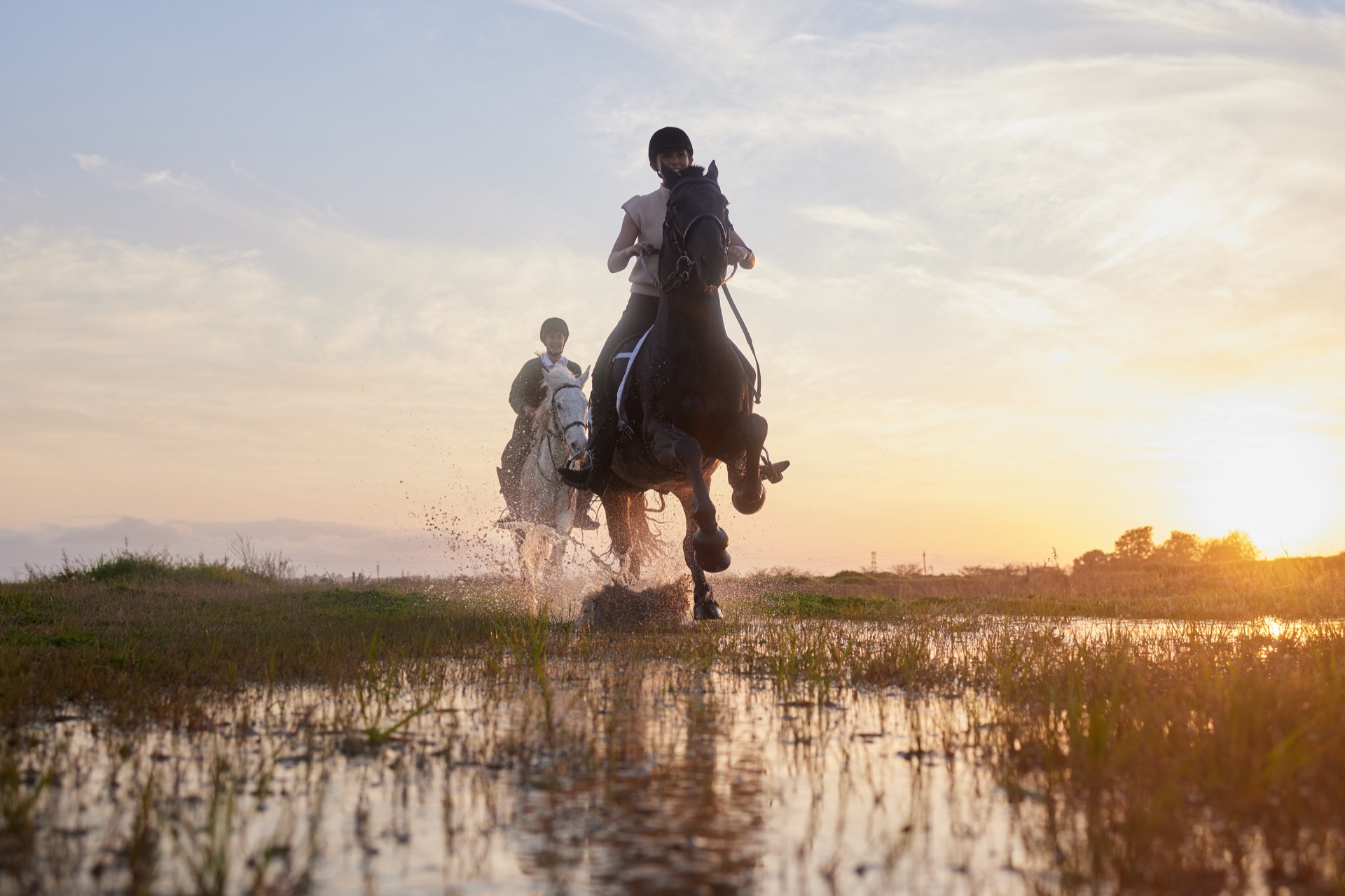 Zwei Reiter mit ihren Pferden im Wasser bei Sonnenuntergang